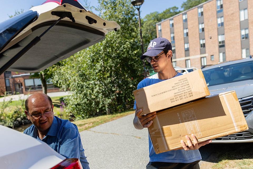 An orientation leader lifts boxes out of the trunk of a car.
