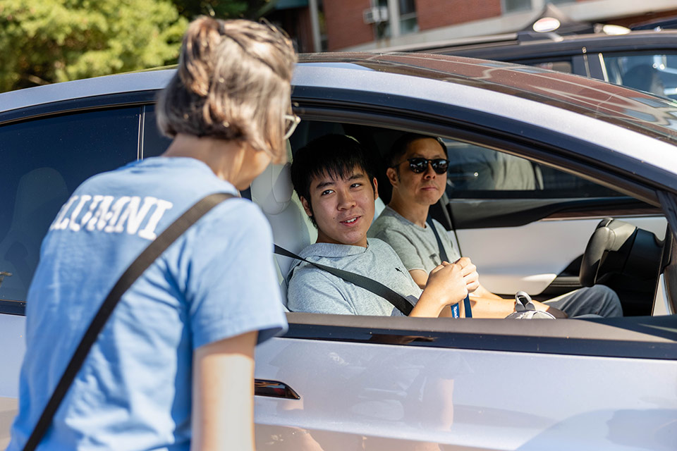 A student and father are greeted in their car by a Brandeis staff member.