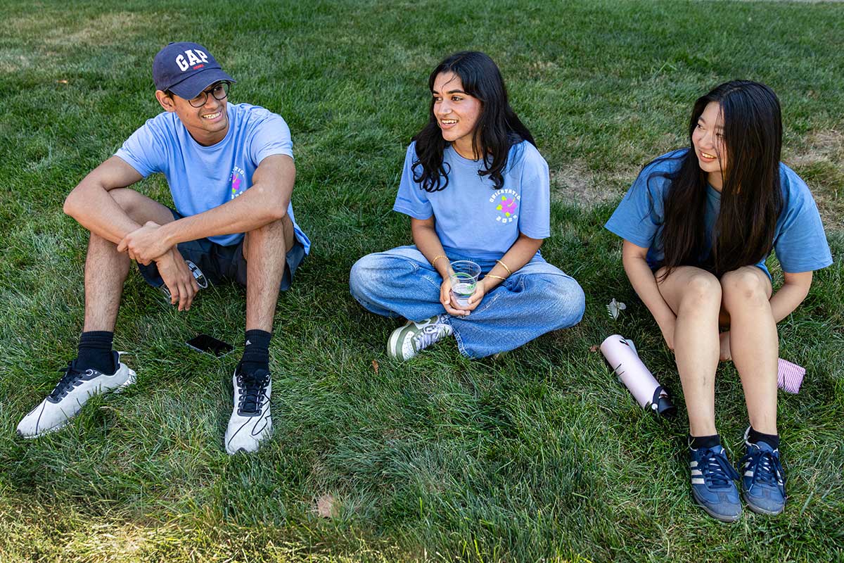 Three orientation leaders sit on the grass outside on campus.