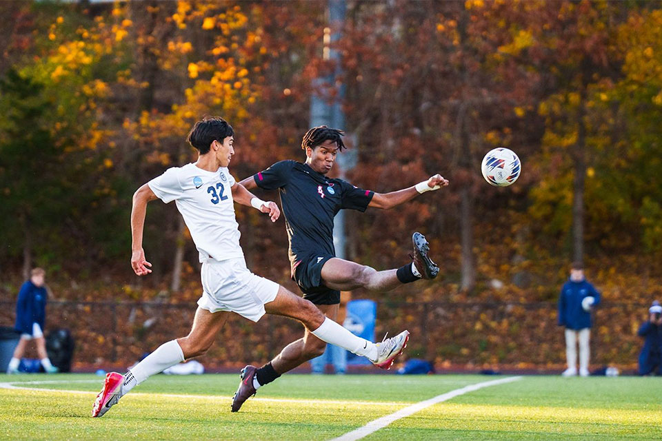 Two soccer players run after a soccer ball.
