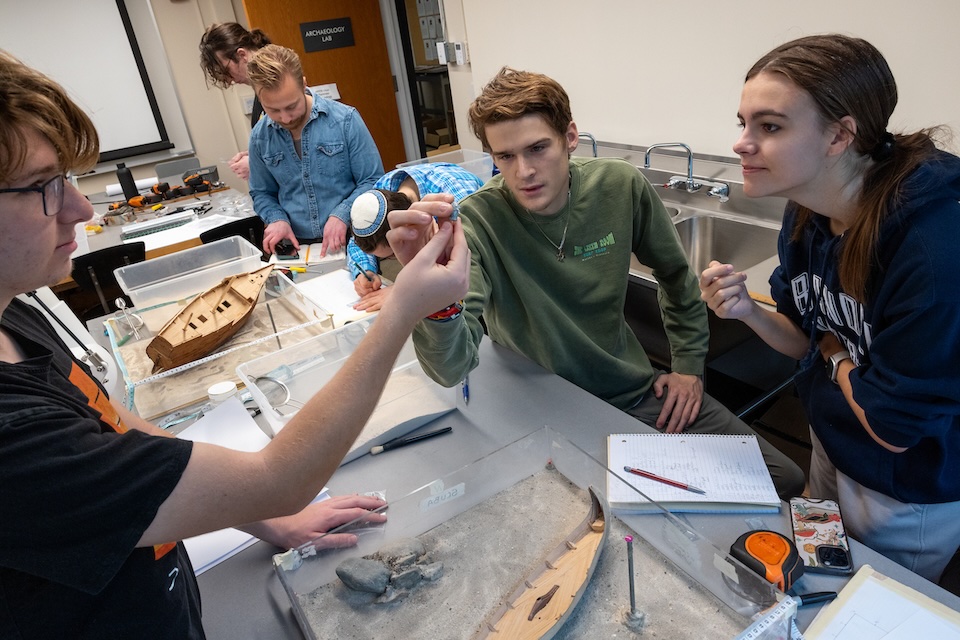 Students inspect a miniature artifact excavated from a model shipwreck.