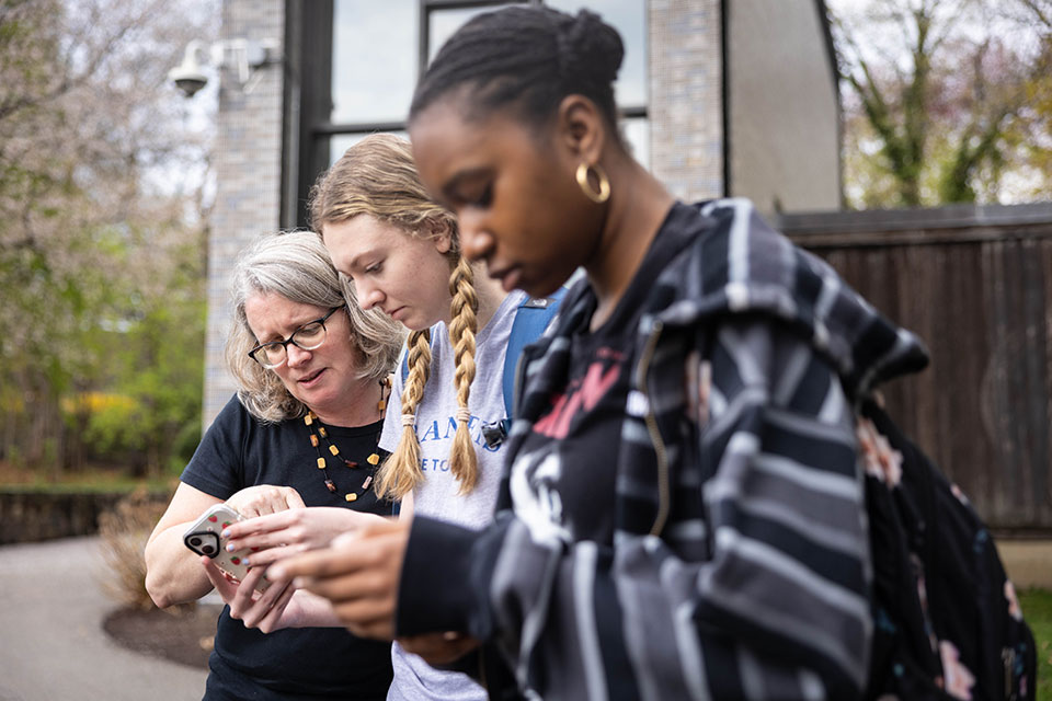 Professor Hitchcock and two students look at a cell phone.