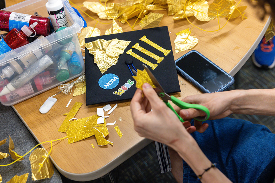 A student decorates their graduation mortarboard.