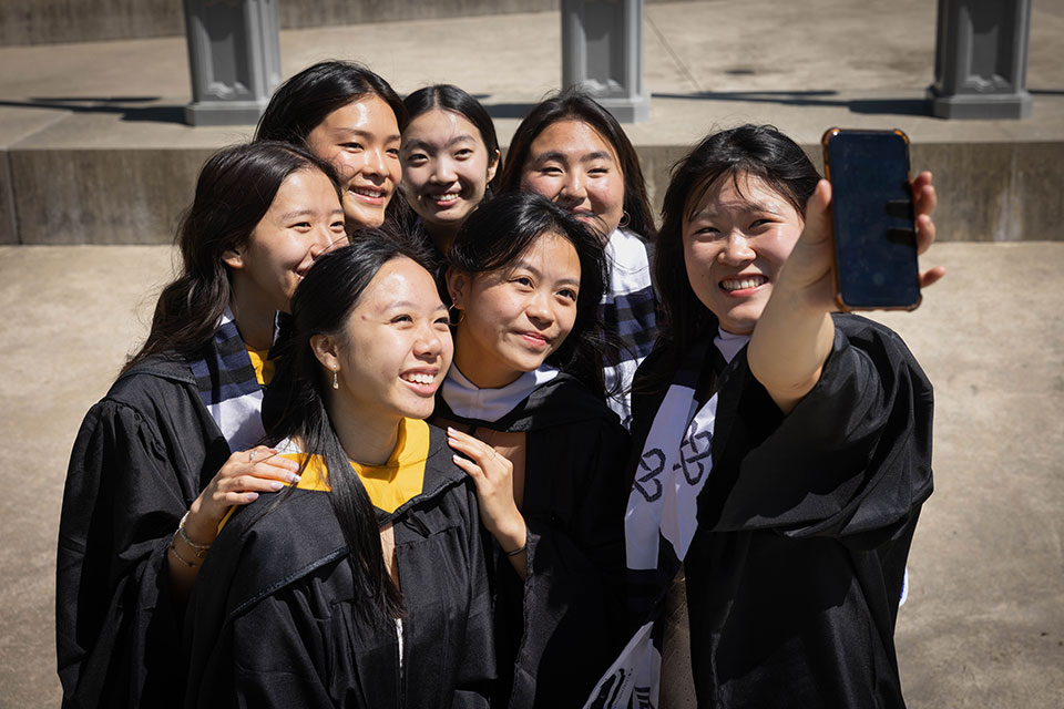 A group of students dressed in academic regalia take a selfie.
