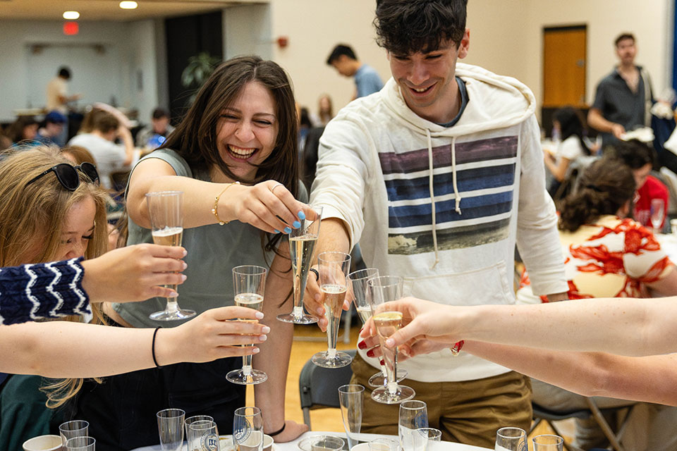 Graduates clink champagne glasses together and laugh.