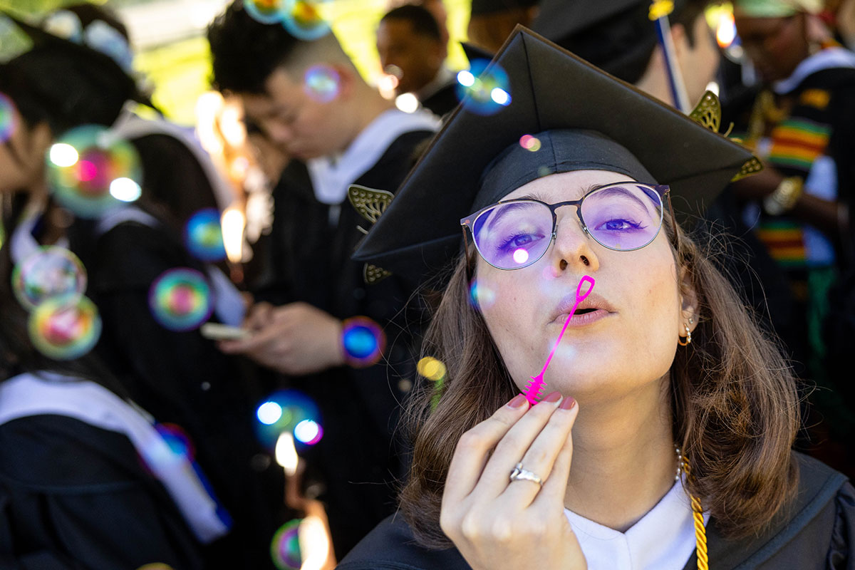 A graduating student wearing academic regalia blows bubbles after the Commencement ceremony.