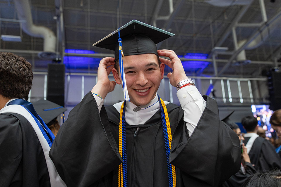 A graduating student wearing academic regalia adjusts their cap.