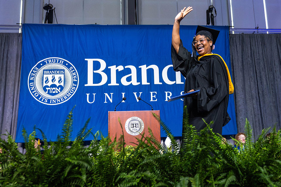A student dressed in academic regalia waves from the stage at Commencement.