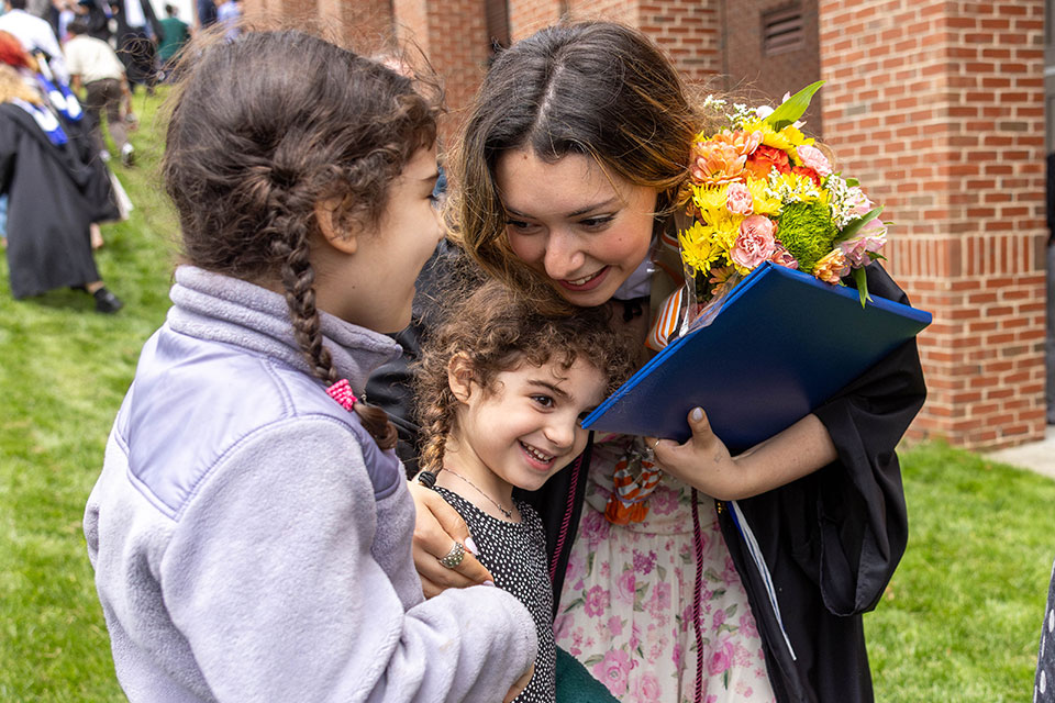 A graduating student hugs two children outside after the Commencement ceremony.
