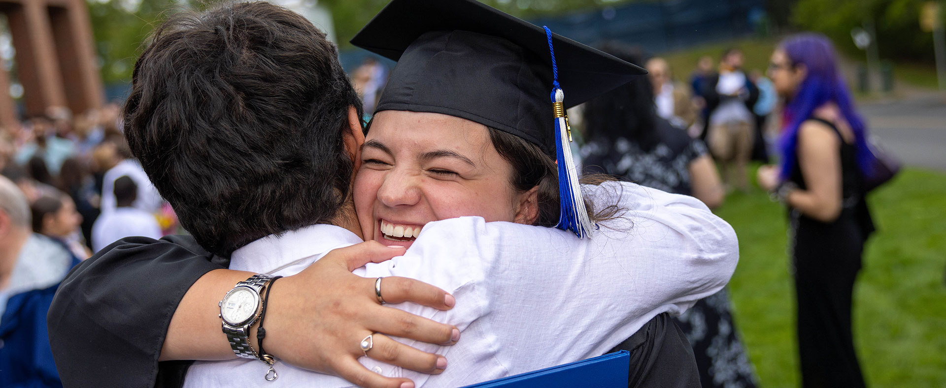 A graduate wearing academic regalia hugs a friend.