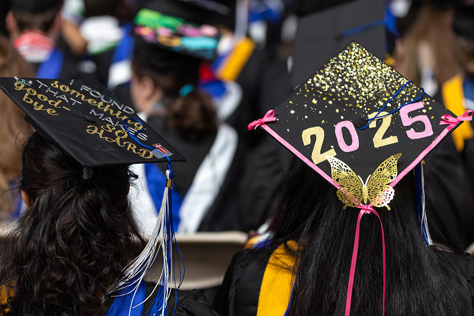 Two graduating students wear hand-decorated mortarboards. One reads "I found something that makes goodbye so hard" and the other reads "2025."