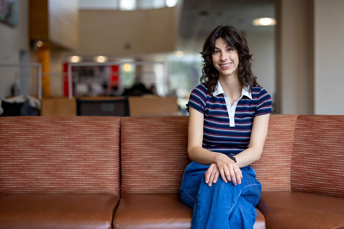 Caterina wears a striped shirt and sits on a brown couch.
