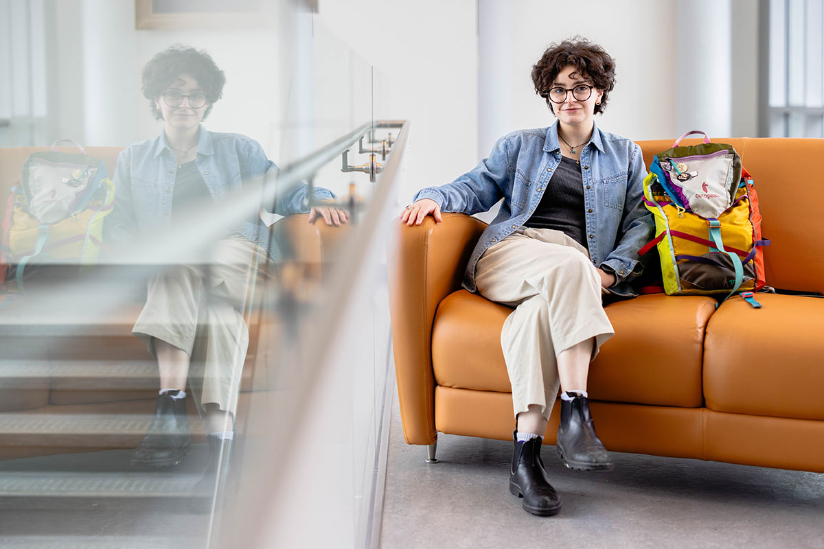 Gonny sits on an orange sofa next to a colorful backpack.