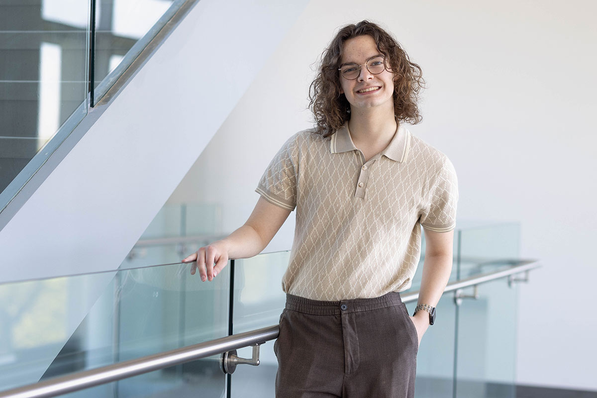 Preston stands next to a glass railing and wears a beige polo shirt.