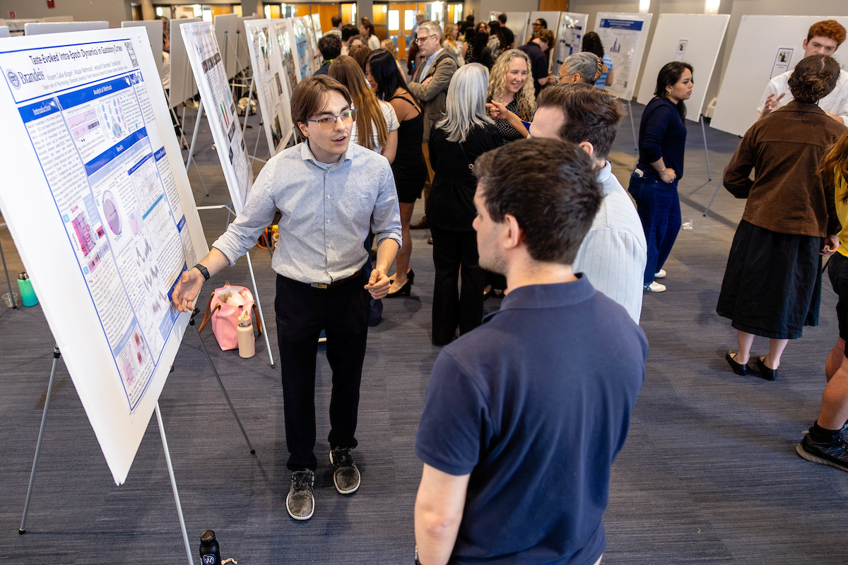 A picture of a woman presenting a scientific poster to an audience