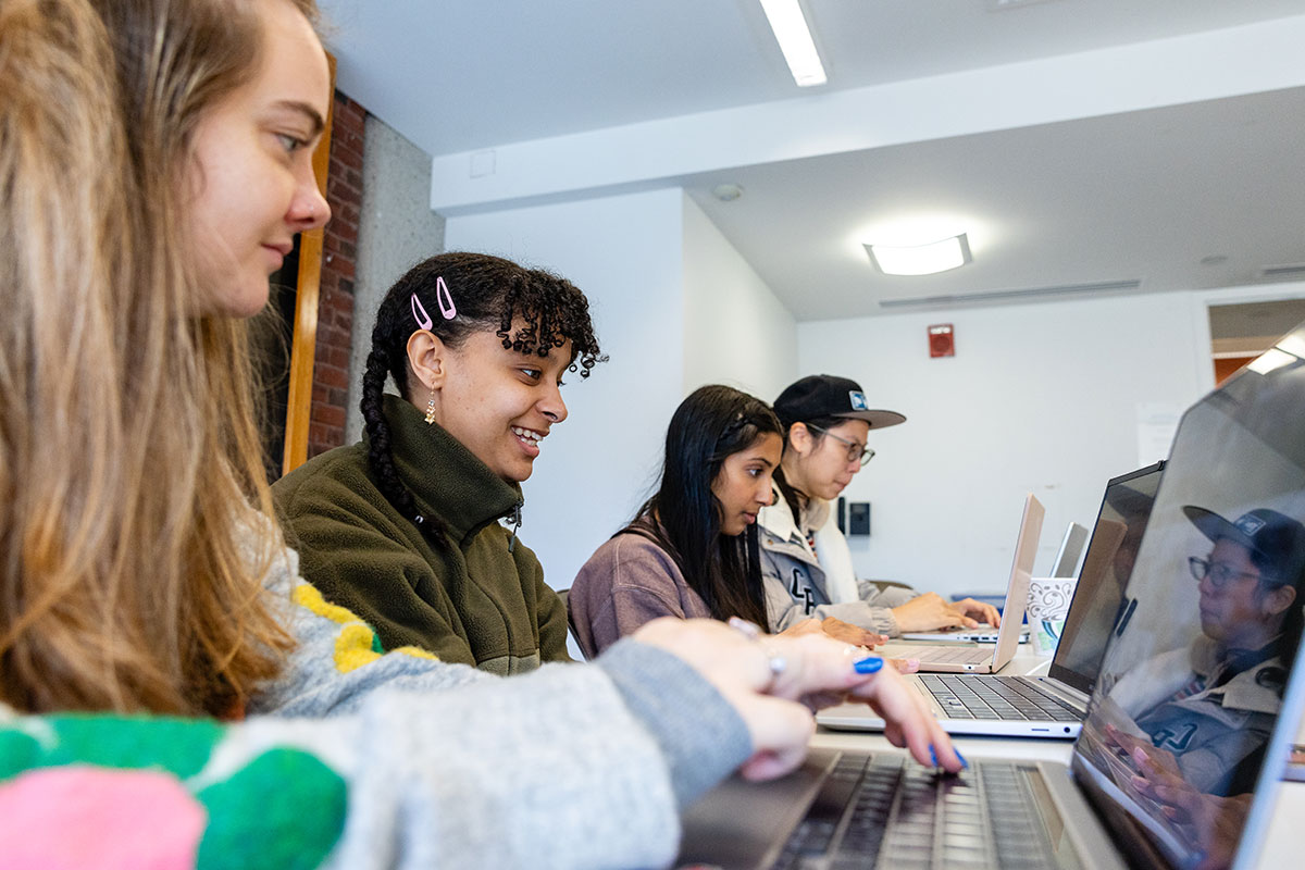 Four students sit in a classroom and work on their laptops.