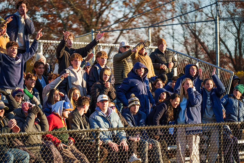 A crowd of Brandeis fans cheers from the bleachers.