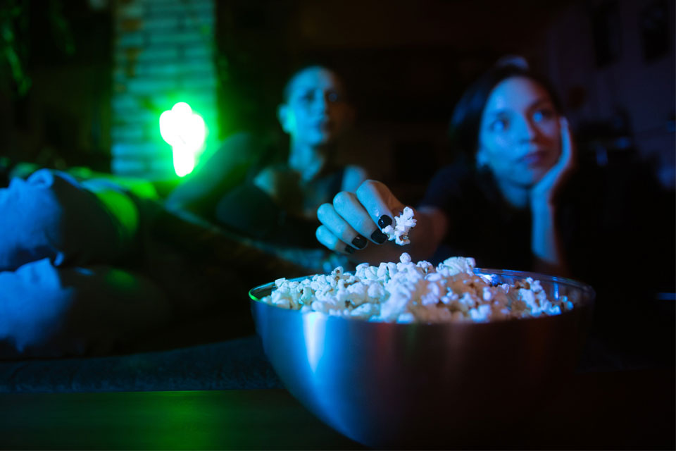 Two people eat popcorn while watching a movie.