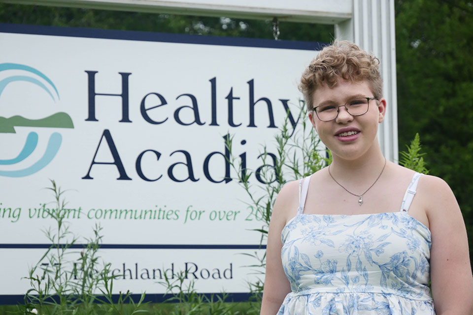 Elizabeth Ford '27 standing in front of the Healthy Acadia sign.