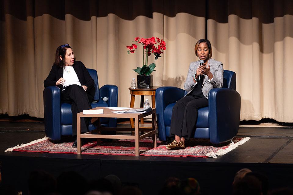Attorney General Campbell and Melissa Stimell sit on stage and address the audience.
