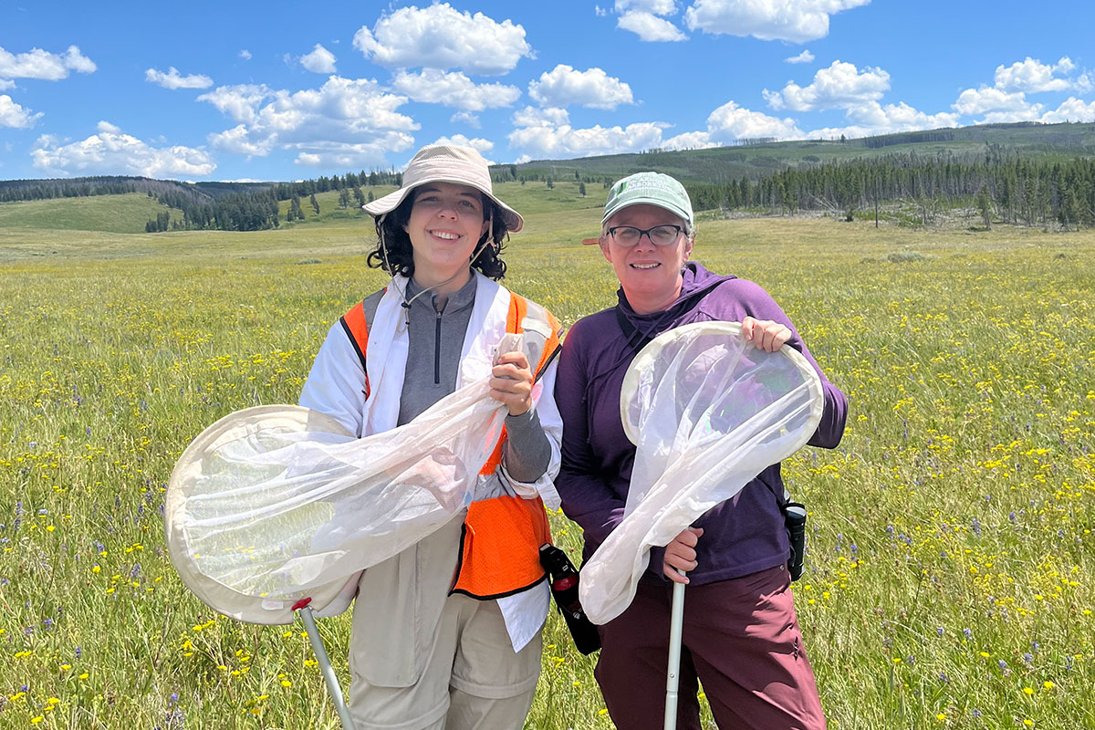 Vivienne Raczkowski and Professor Colleen Hitchcock stand outside in a field holding nets.