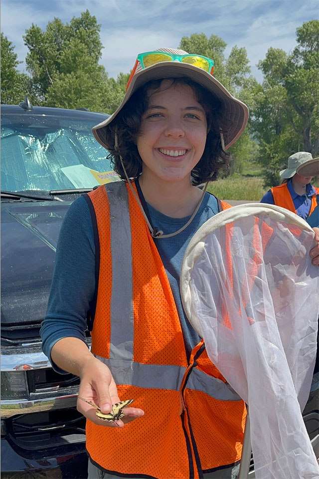 Vivienne Raczkowski stands outside holding a net and wearing a high visibility vest.