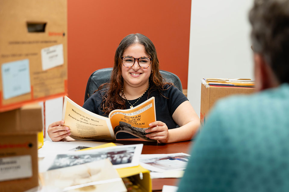 Gabriella Chiquiar-Rabinovich sitting at a table surrounded by files and boxes at the Jewish Women’s Archive