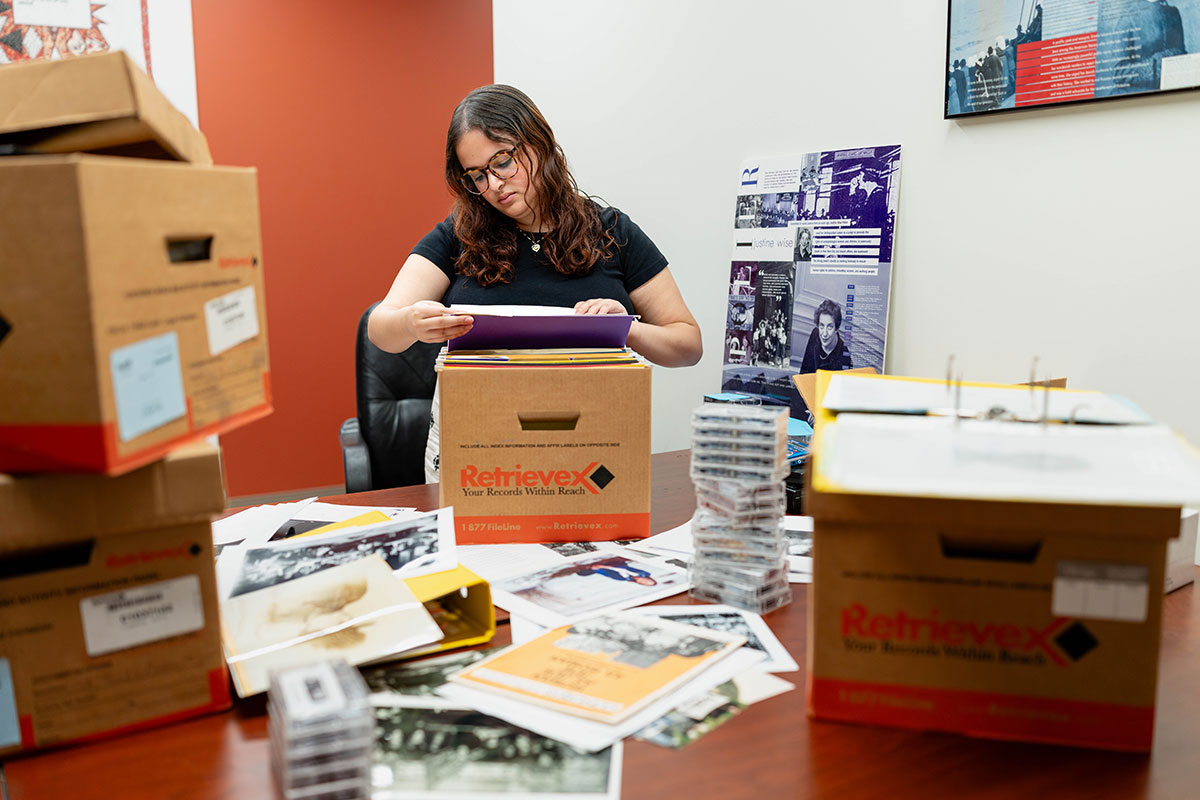 Gabriella Chiquiar-Rabinovich stands at a table covered in files and reads a document.