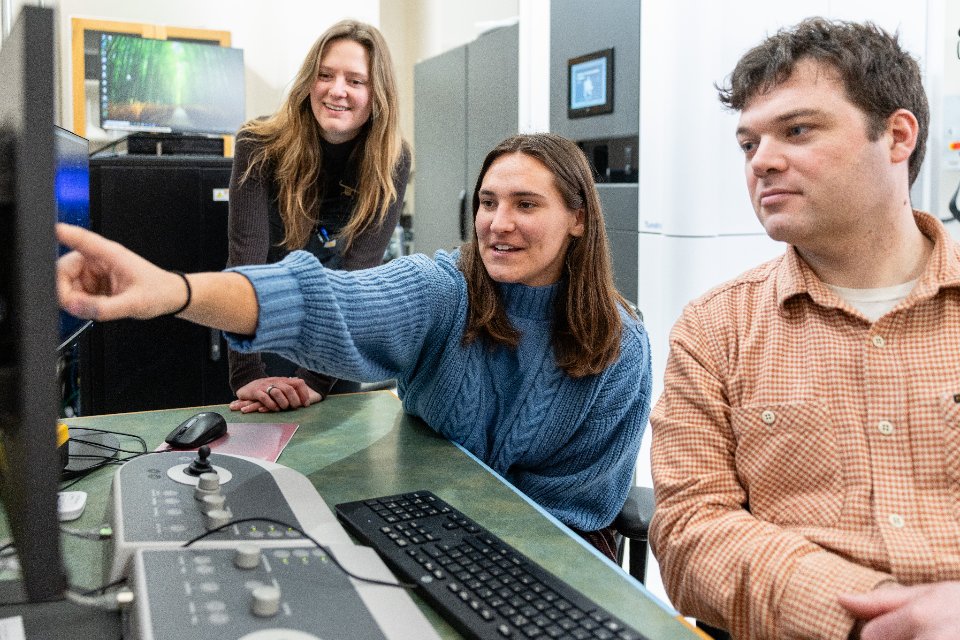 Two students and a professor pointing to a computer screen.