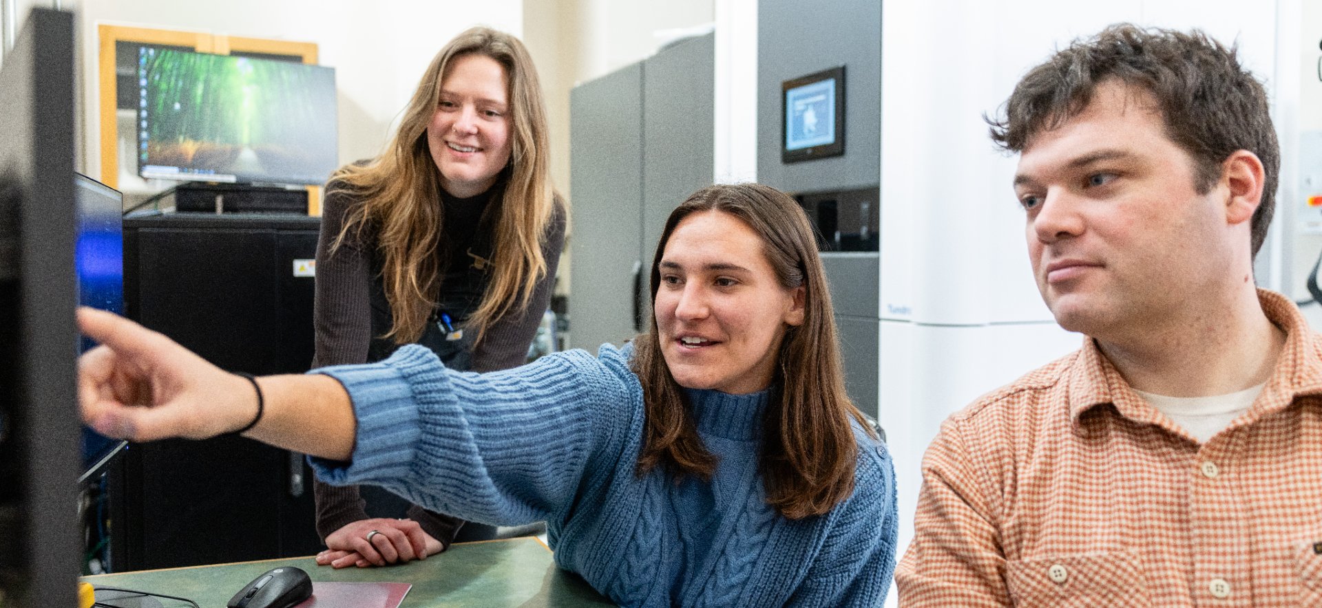 Two students and a professor pointing to a computer screen.