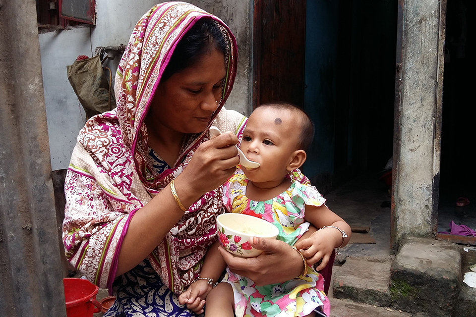 a mother feeding a sick child that is sitting on her knee