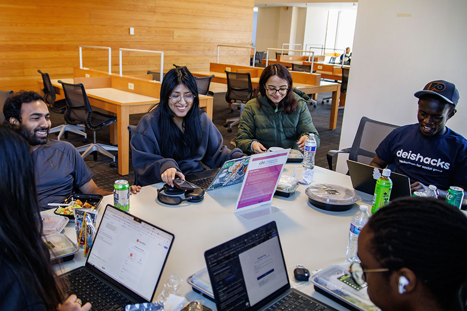 A group of students sit around a table and work on their computers during DeisHacks 2026.