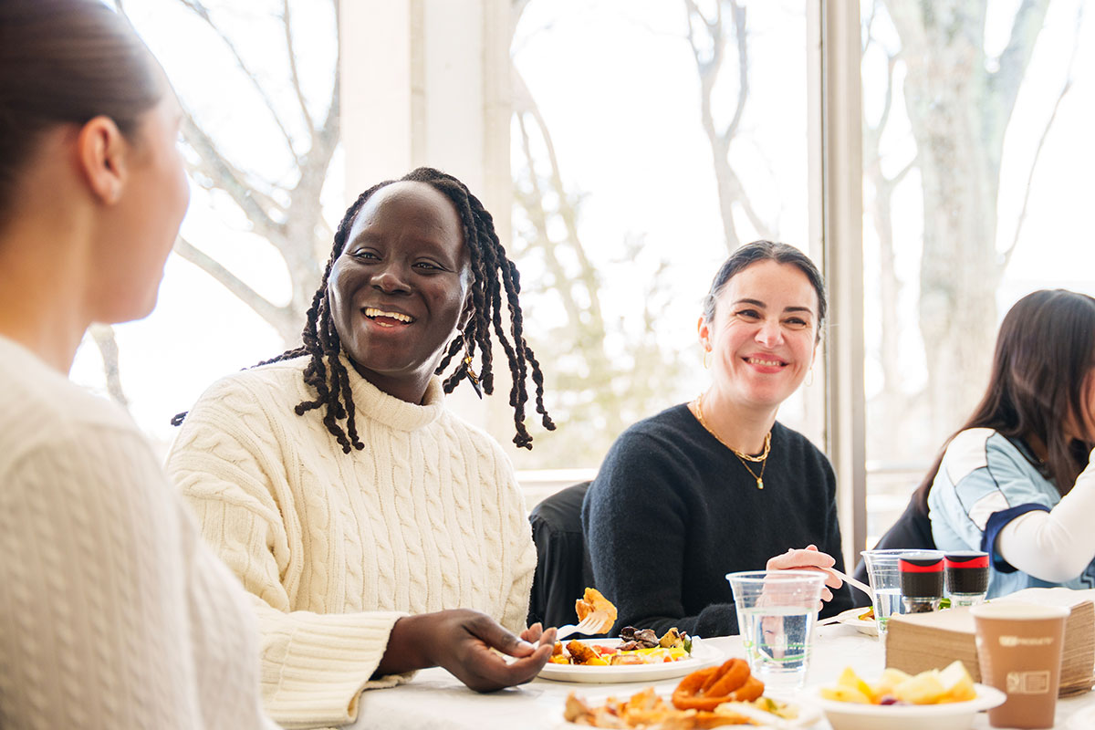 Professors Emilie Diouf and Sarah Mayorga speak with students at a lunch table.