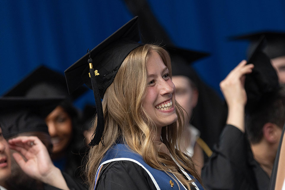 A graduating student dressed in academic regalia smiles.