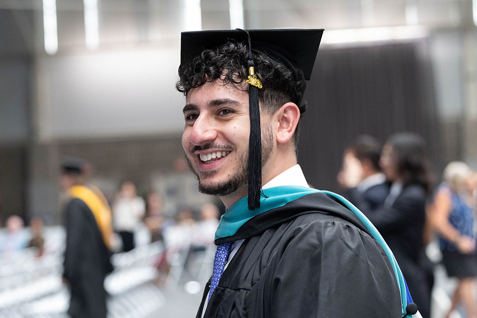 A graduating student dressed in academic regalia smiles.
