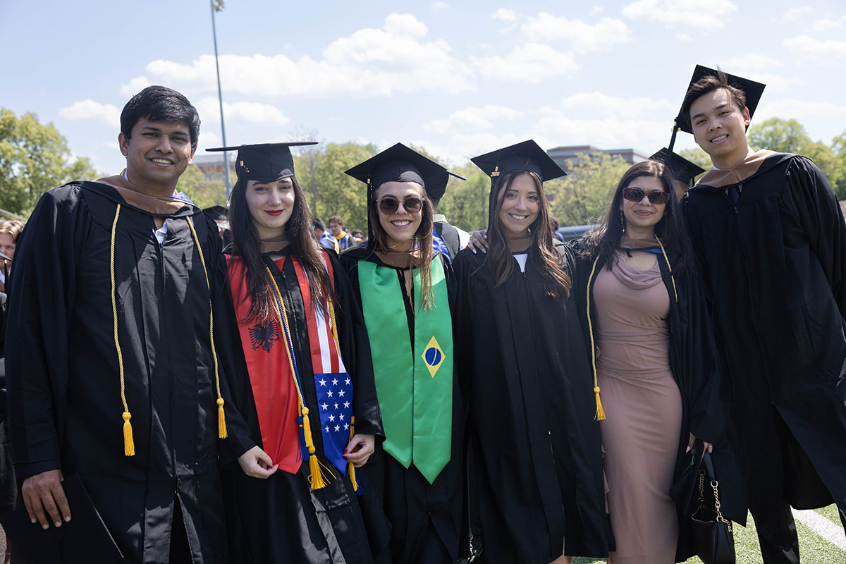 A group of graduating students pose together for a photo outside.