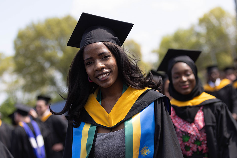 A student dressed in academic regalia smiles outside.