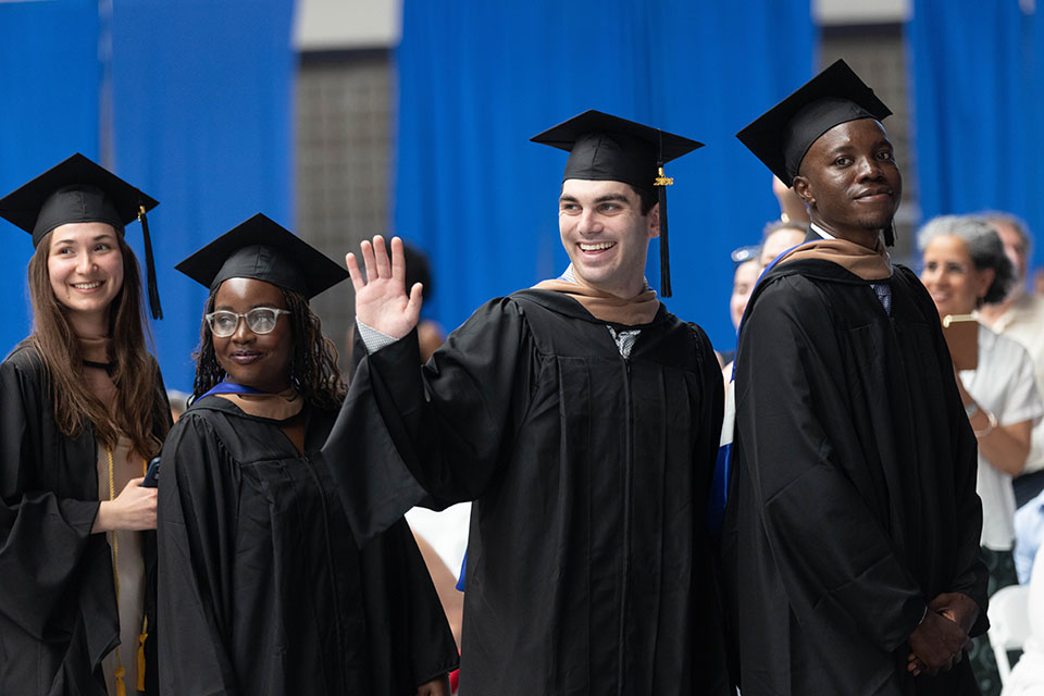 Graduating students walk in a line and wave.