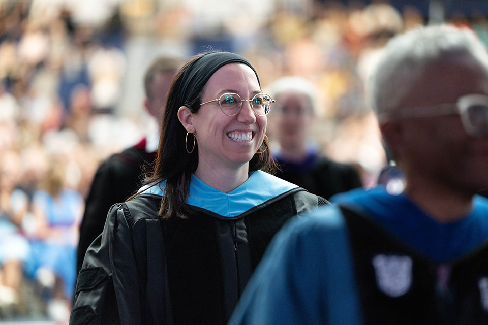 A student dressed in commencement regalia smiles.