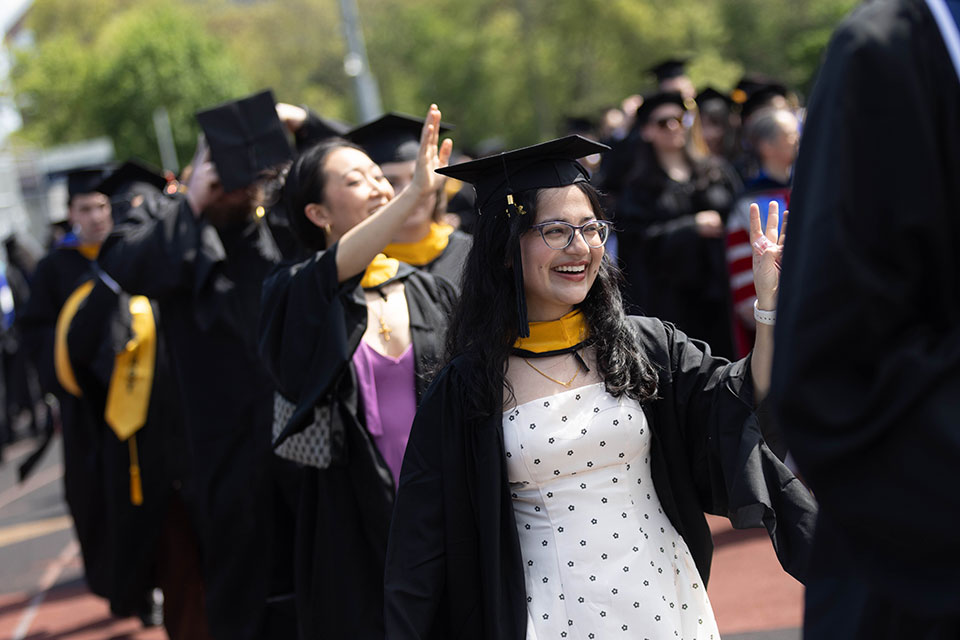 Graduating students dressed in academic regalia walk and wave.