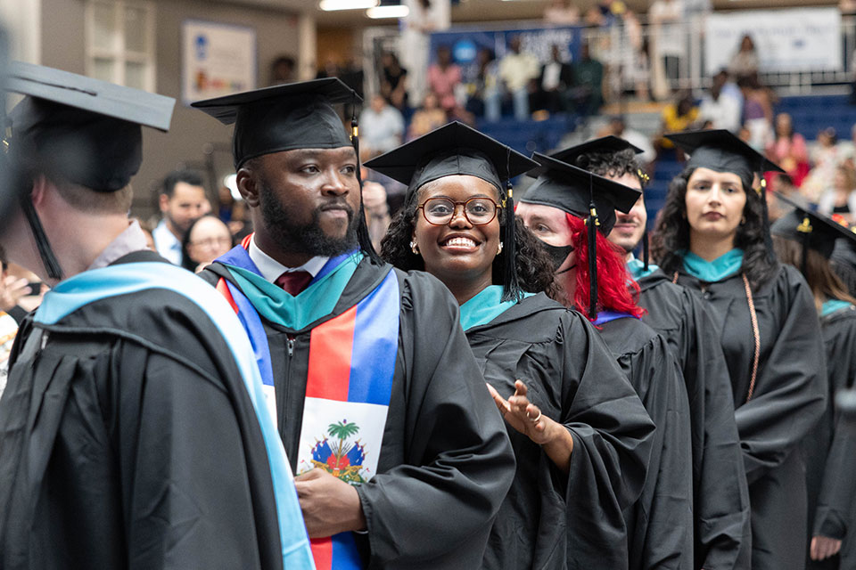 Graduating students dressed in academic regalia smile at the graduate commencement ceremony.