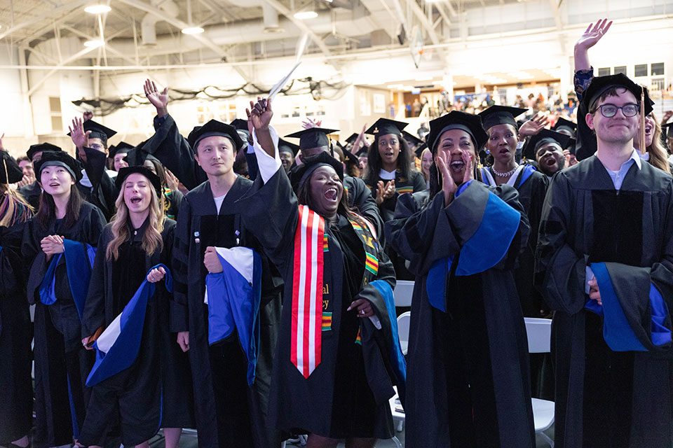 An audience of graduate students applaud and celebrate.
