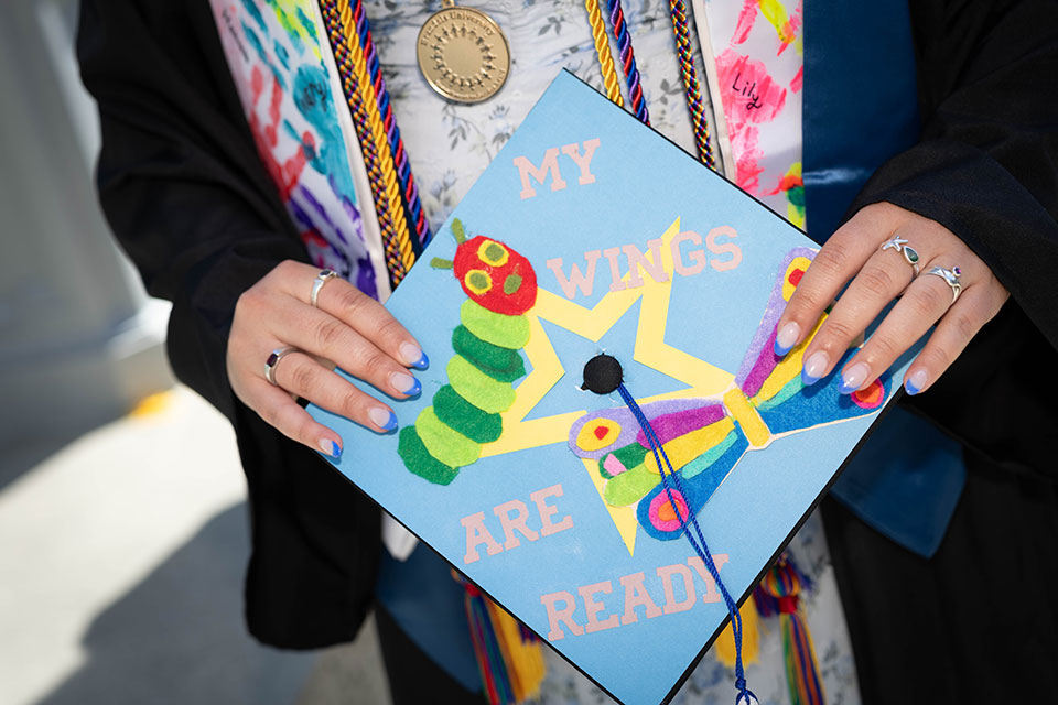 A soon-to-be-graduate's graduation cap decorated with a photo of a caterpillar and butterfly with the words "My wings are ready."