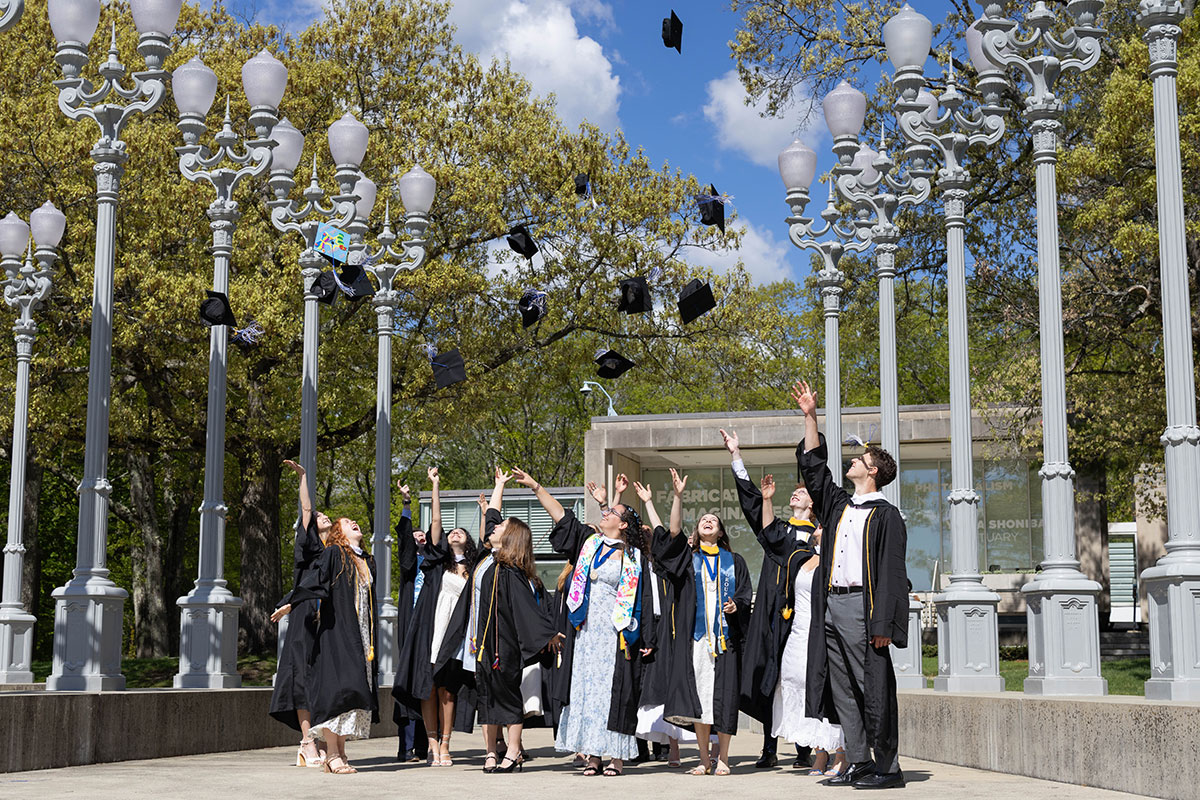 A group of graduates dressed in academic regalia throw their caps in the air.