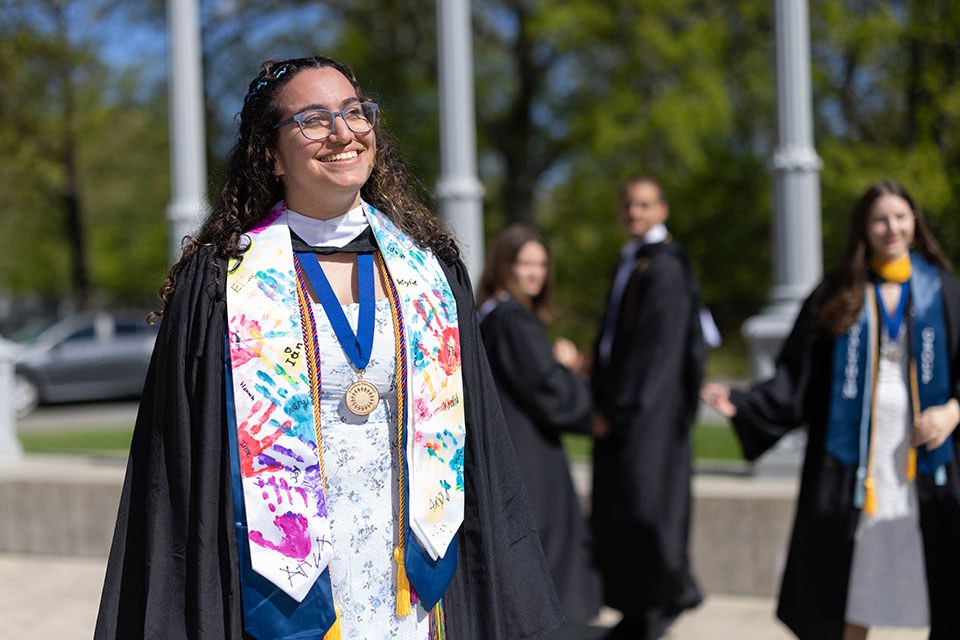 A student dressed in academic regalia smiles. 
