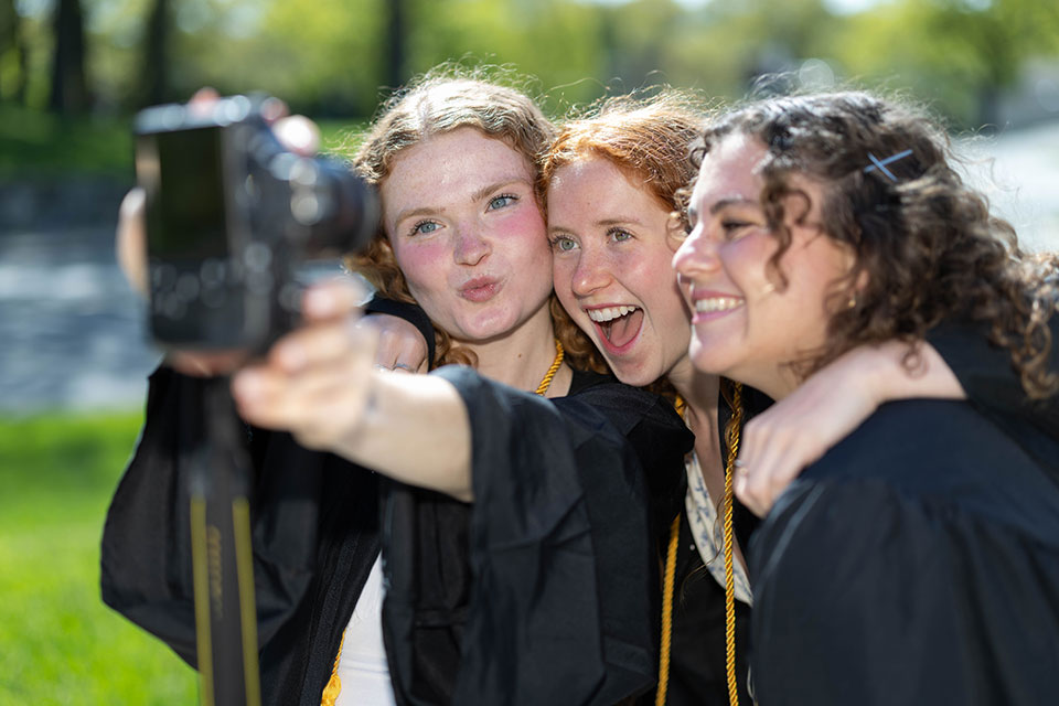 Three graduating students take a selfie with a digital camera.