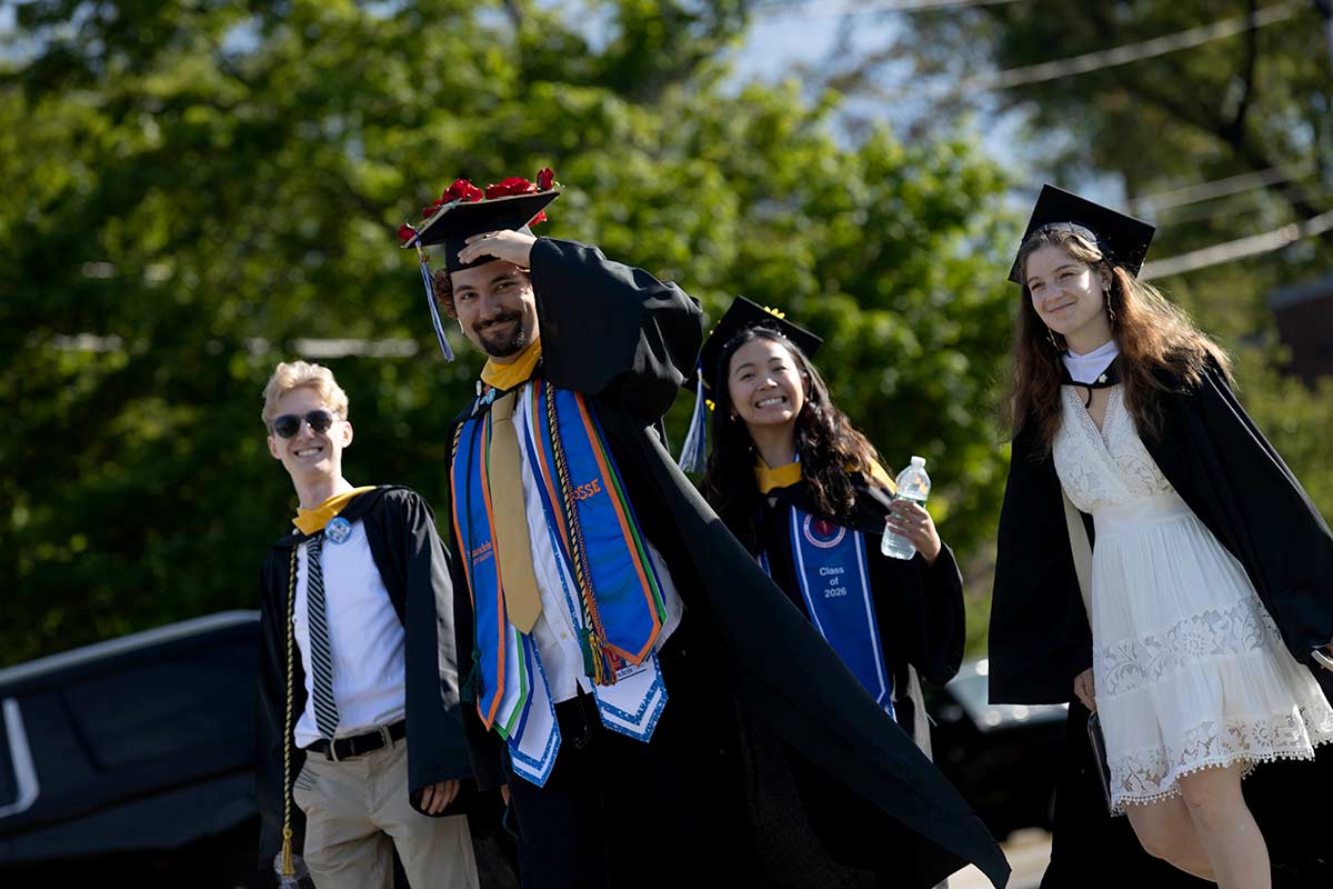 Four graduating students dressed in academic regalia smile ourside