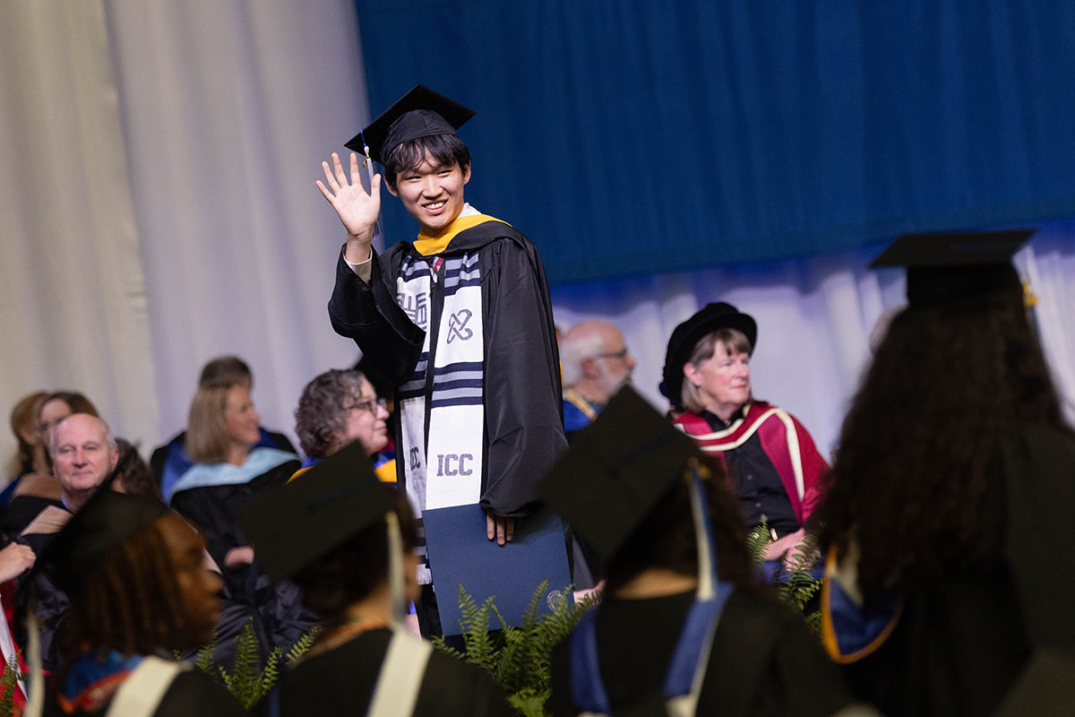 A graduate waving while crossing the stage