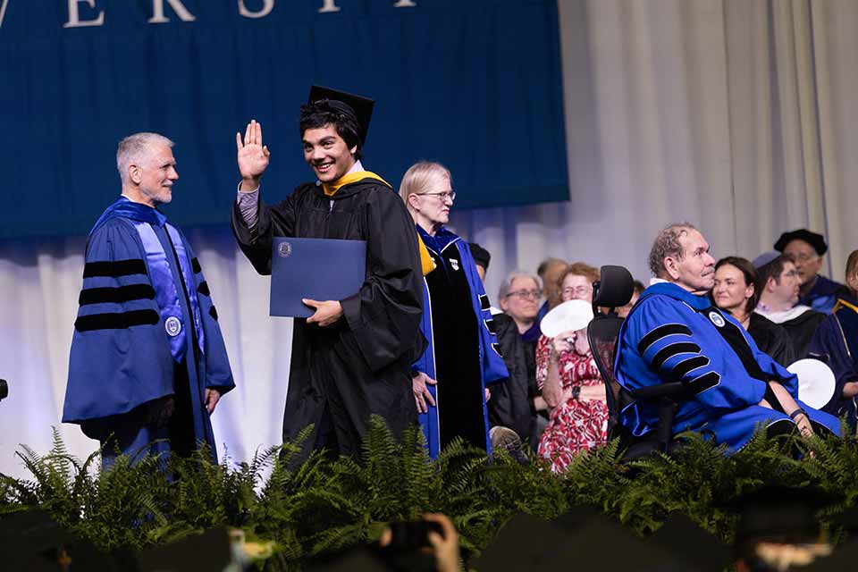 A graduate waves while crossing the stage
