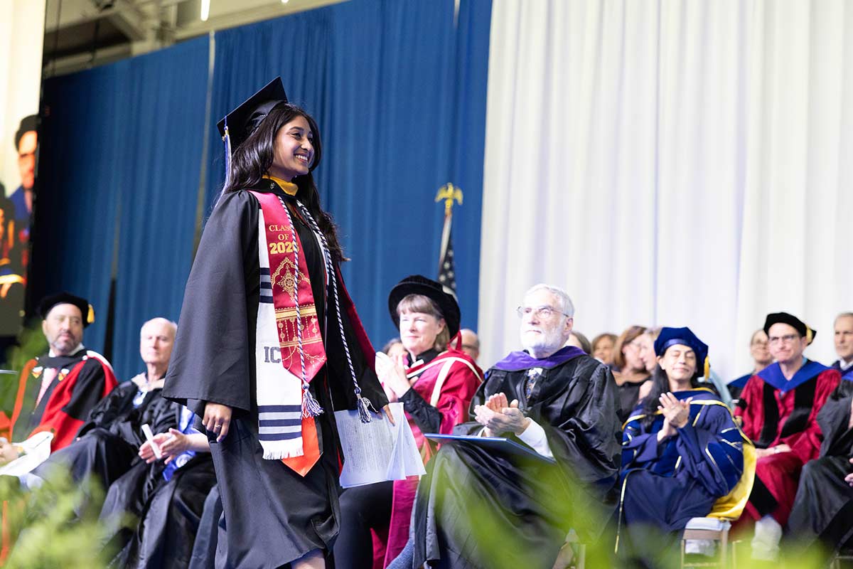 Khimaya Bagla dressed in academic regalia, walks across the stage at Commencement